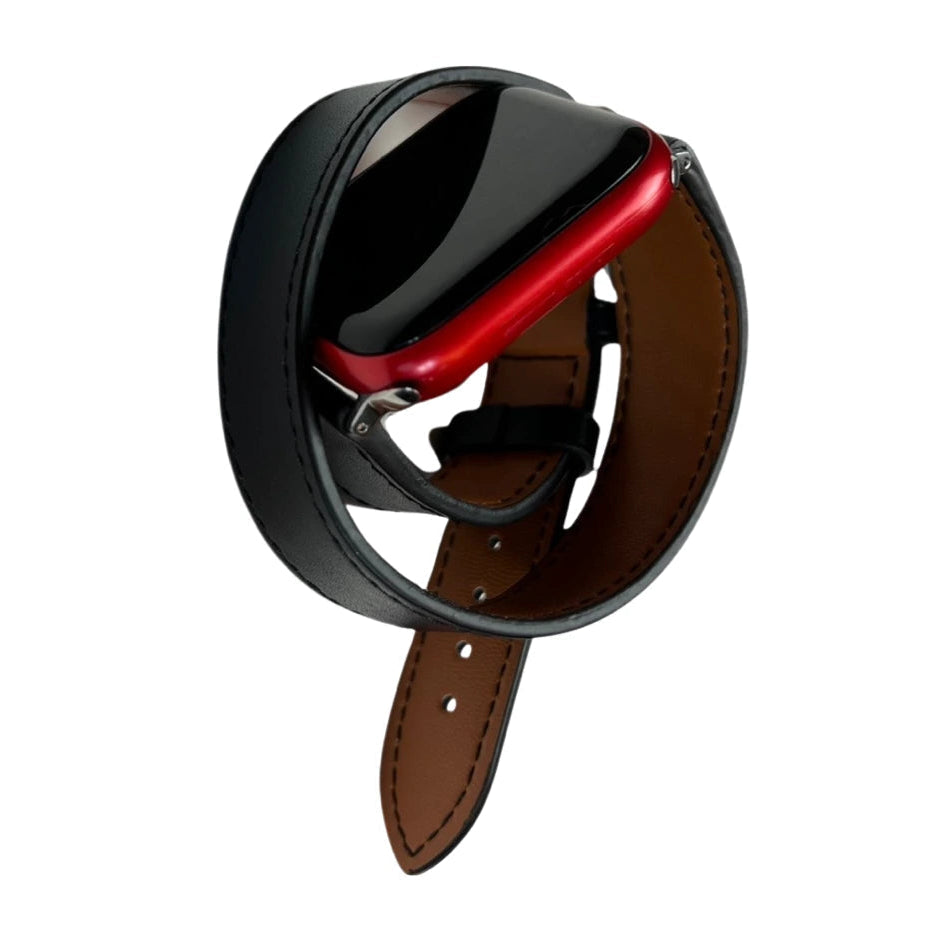 A black leather watch strap with a brown interior lining and a red metal buckle.