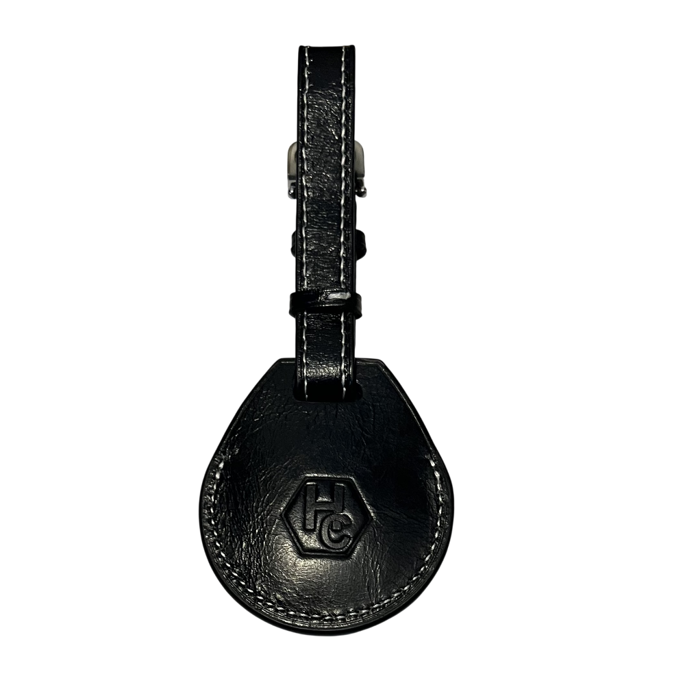 A black leather AirTag holder with a teardrop-shaped body and a matching strap, featuring an embossed 'HC' logo 