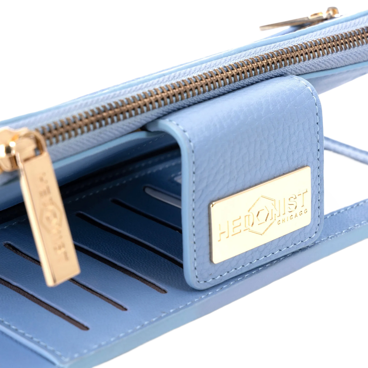 A close-up of a light blue leather wallet or clutch with gold-tone hardware, including a zipper, pull tab, and a gold-tone metal brand plaque that reads 'HEDONIST CHICAGO'.