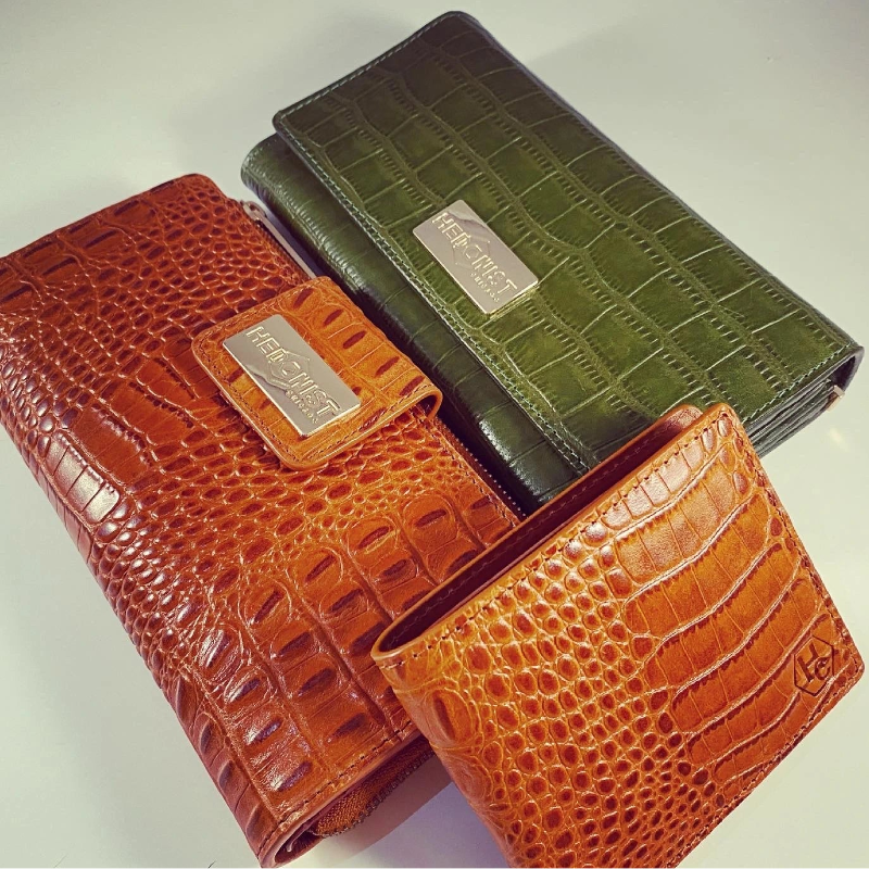 Two crocodile skin wallets, one brown and one green, on a light background.