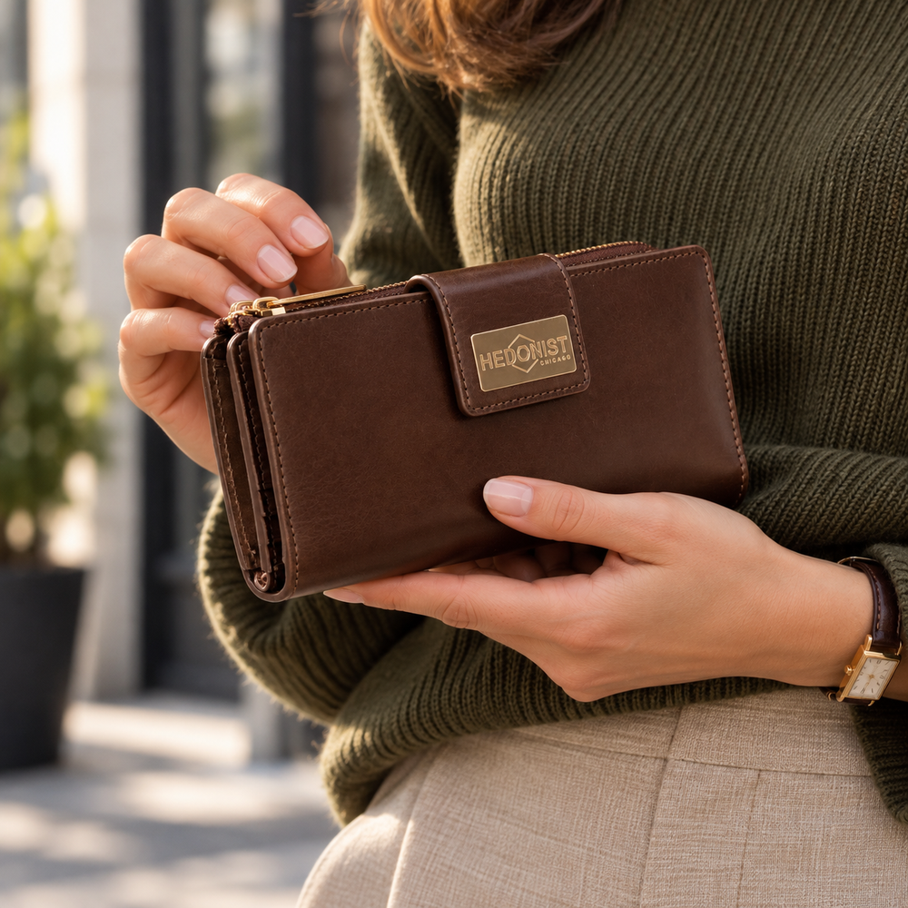 A woman in an olive green sweater holds a brown leather wallet with a gold-tone logo plate reading Hedonist Chicago.