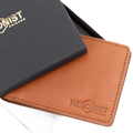 A tan leather bifold wallet with an embossed Hedonist Chicago logo, shown next to its black presentation box with gold lettering.