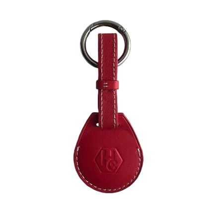 A red leather AirTag Holder with a teardrop-shaped tag, white contrast stitching, and a silver metal key ring, featuring an embossed logo on the tag.