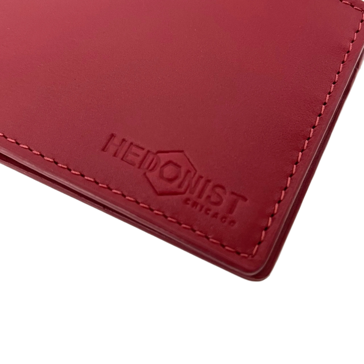 A close-up of a red leather wallet corner with matching red stitching and an embossed logo reading 'HEDONIST CHICAGO' on a white background.