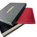 A red leather wallet with an embossed logo, shown partially inside a black presentation box with a gold-embossed logo on a white background.