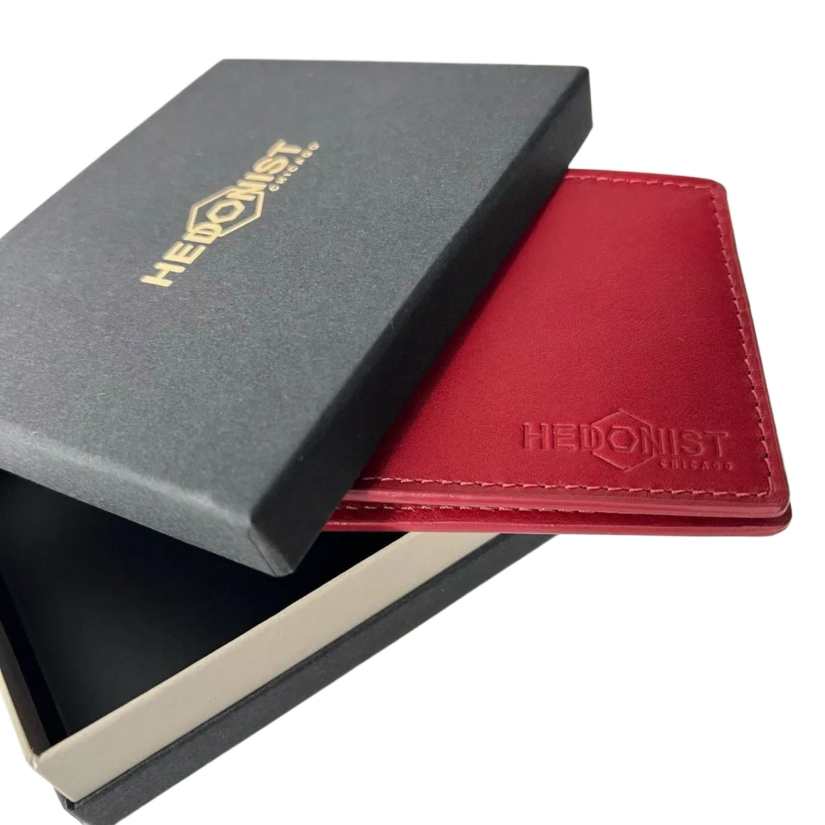 A red leather wallet with an embossed logo, shown partially inside a black presentation box with a gold-embossed logo on a white background.