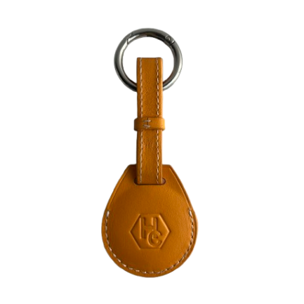 A yellow leather AirTag Holder with a teardrop-shaped tag and a silver metal key ring, featuring an embossed 'HG' logo on the front