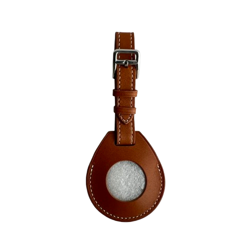A brown leather AirTag Holder with a teardrop-shaped body, a circular gray felt insert, and a matching brown leather strap with a silver buckle
