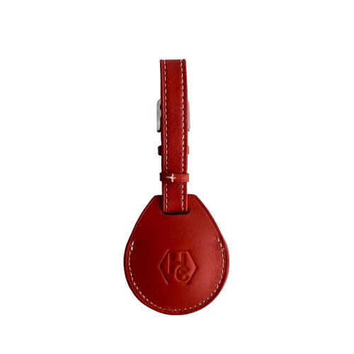A red leather AirTag Holder with a teardrop-shaped tag and a matching strap, featuring a debossed logo on the front