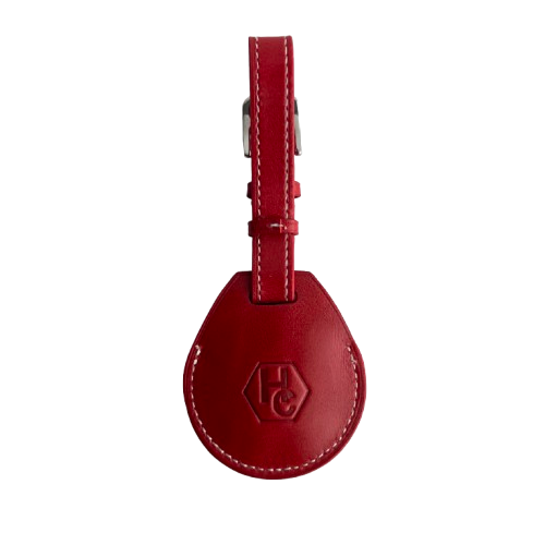A red leather AirTag Holder with a teardrop-shaped body, white contrast stitching, and a silver metal buckle, featuring an embossed 'HC' logo on the front.