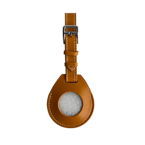 A tan leather lAirTag Holder with a teardrop-shaped body, a circular fabric window, and a silver metal buckle on a white background.