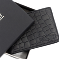 A black crocodile-embossed leather wallet shown partially open next to its black presentation box. The brand name 'HEDONIST Chicago' is debossed on the lower right corner of the wallet.