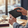 Person holding a black minimalist wallet with a blurred cafe background