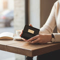 Person holding a black wallet with 'Hedonist Chicago' branding at a table with a blurred background