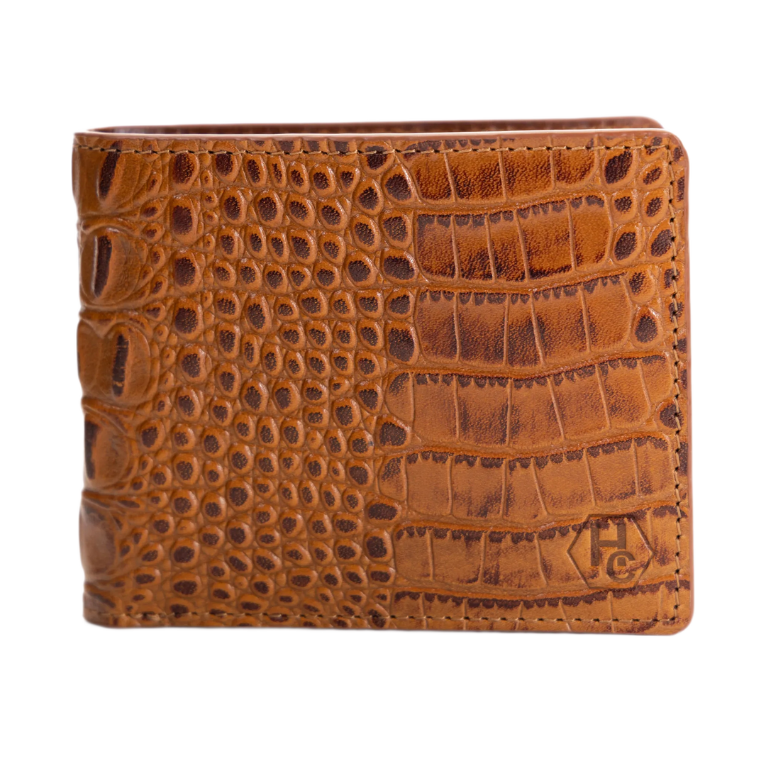A brown crocodile-embossed leather bifold wallet with a stitched edge and a debossed monogram logo in the bottom right corner, shown against a plain white background.