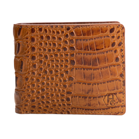 A brown crocodile-embossed leather bifold wallet with a stitched edge and a debossed monogram logo in the bottom right corner, shown against a plain white background.