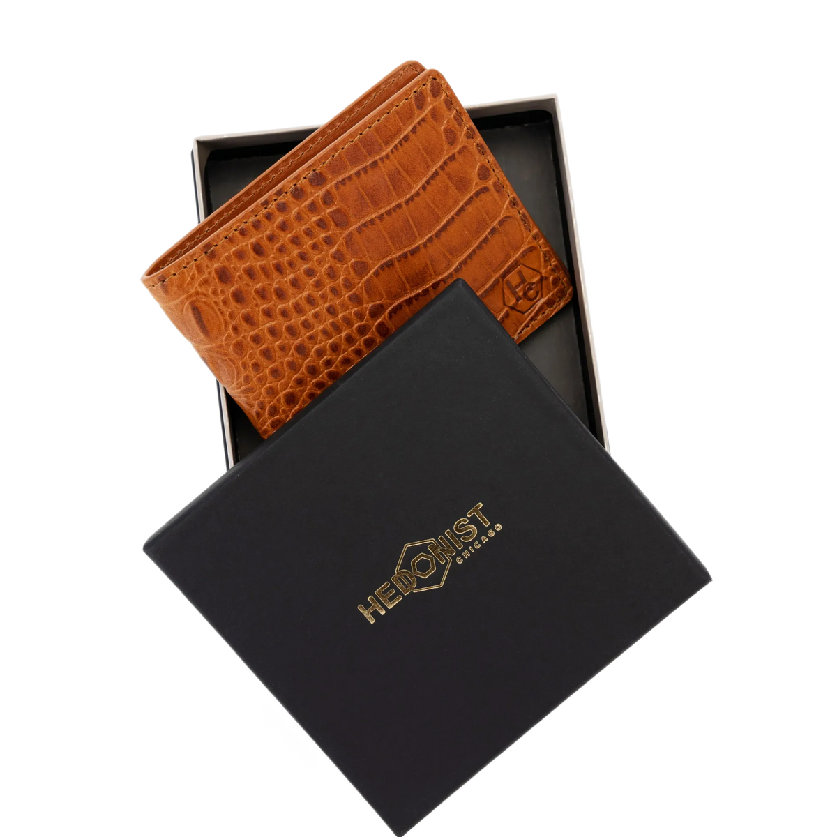 A brown crocodile-embossed leather wallet displayed inside an open black presentation box, with the brand box lid placed in front. 