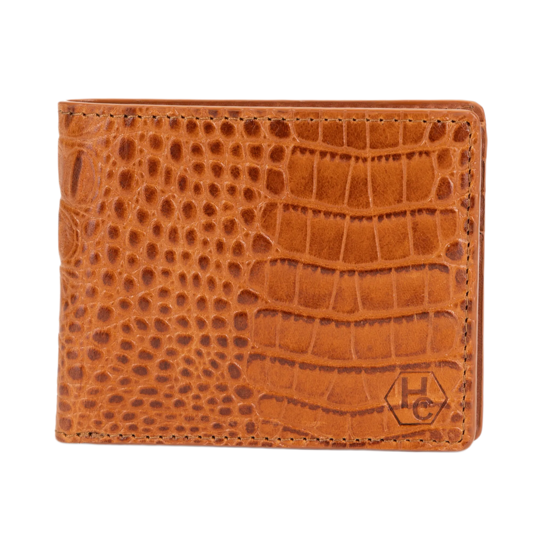 A brown bi-fold wallet with a crocodile-embossed texture, featuring a small embossed 'HC' logo in the bottom right corner, set against a plain white background.