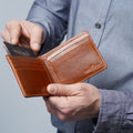 A person holding an open brown croco leather bifold wallet, inserting a card into a slot
