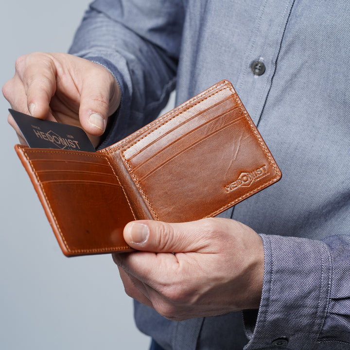 A person holding an open brown croco leather bifold wallet, inserting a card into a slot