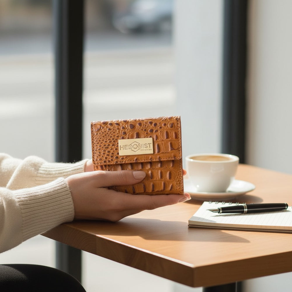 Person holding a brown textured wallet with 'HEDANIST CHICAGO' branding, next to a cup of coffee and notebook on a table.