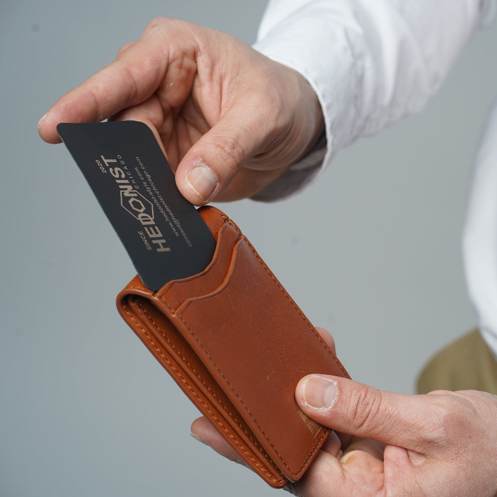A close-up of a person's hands holding a slim brown leather card holder wallet