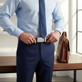 Man adjusting his belt in a professional setting with a briefcase on a table.