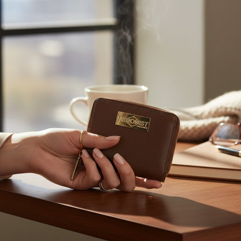 Hand holding a brown leather wallet with a visible brand logo on a wooden table.