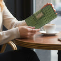 Woman holding the green croco-embossed leather travel wallet with coffee on a table