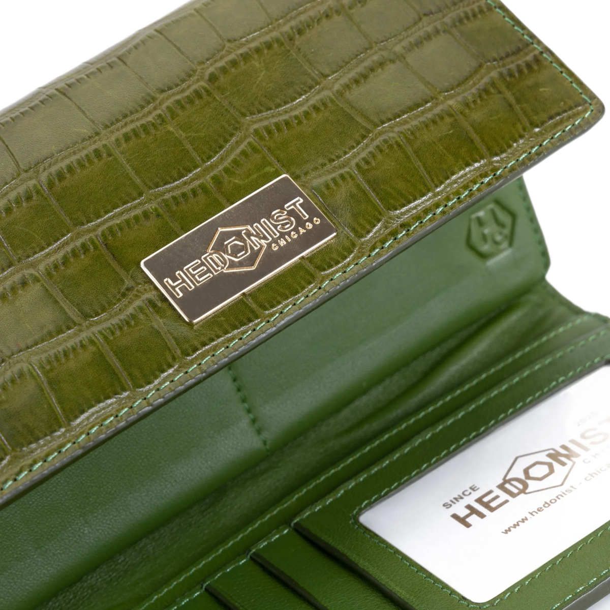 Close-up of green croco-embossed leather trifold wallet showing gold-tone brand plaque and ID window