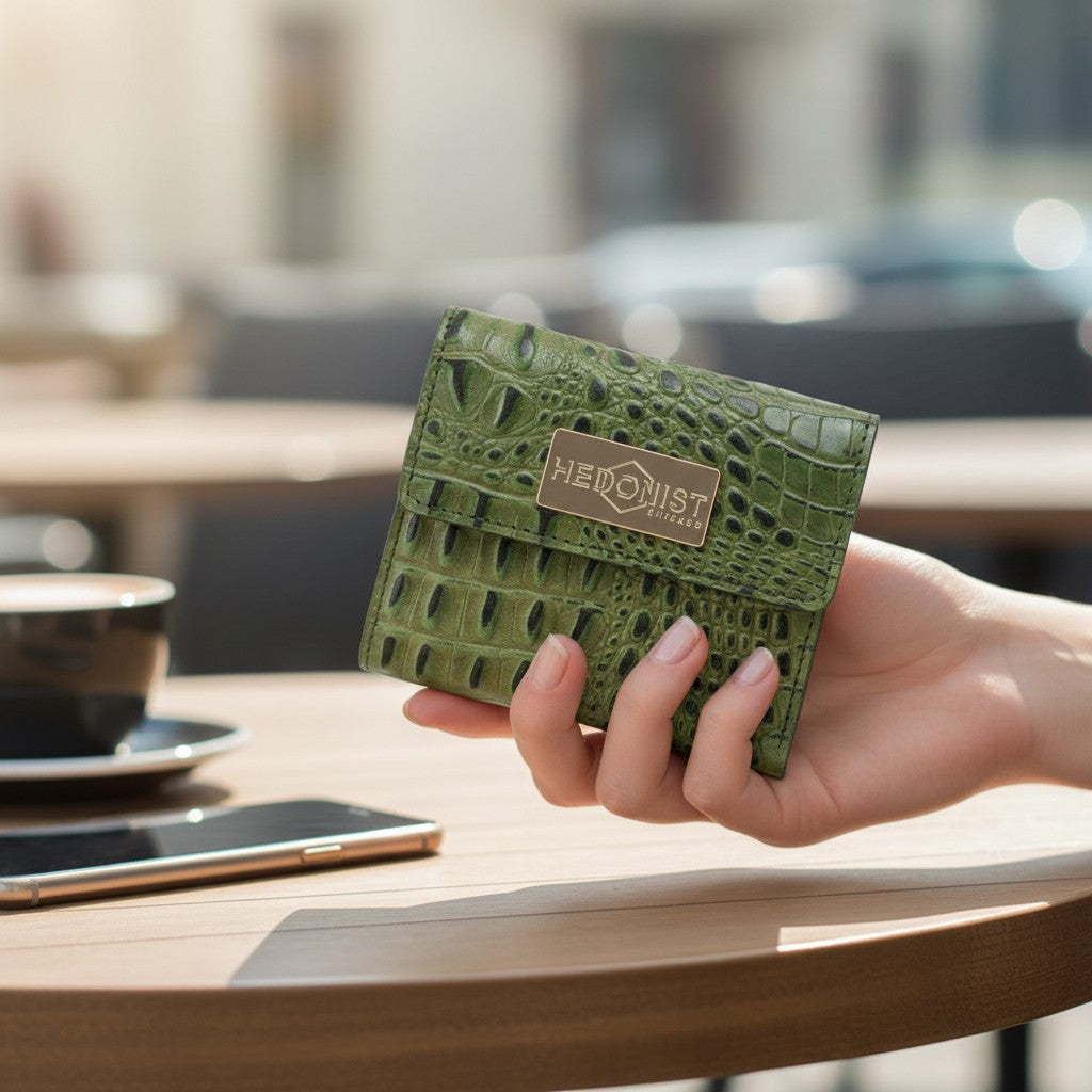 Green crocodile-patterned wallet held by a hand on a blurred outdoor background