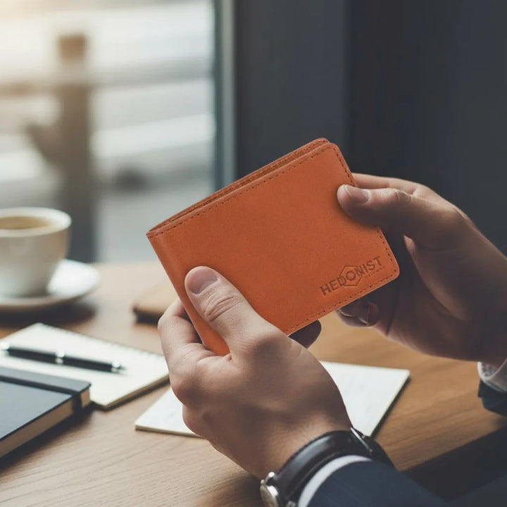 Guy is holding a tan men's wallet with 'HERONIST CHICAGO' branding on a blurred desk background