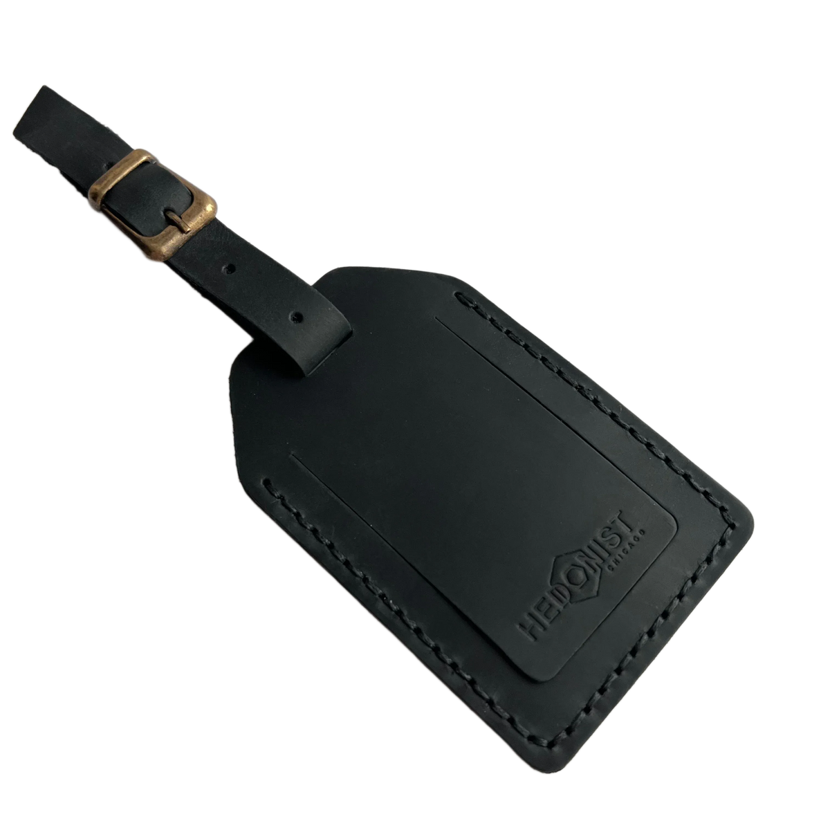 Black full-grain leather luggage tag with brass buckle strap, embossed Hedonist Chicago logo in the lower right corner, shown on a white background.