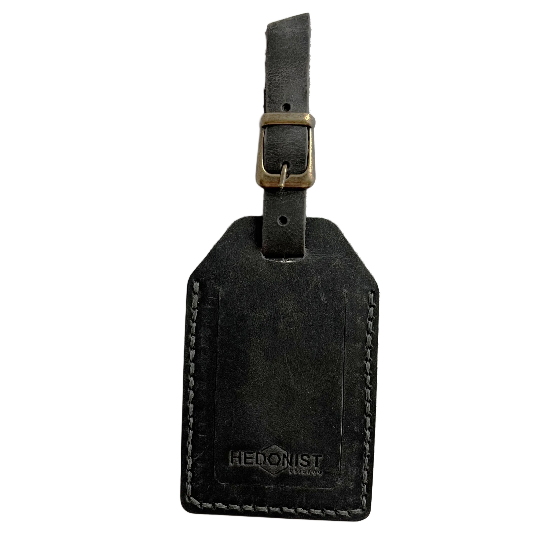 Black washed full-grain leather luggage tag with brass buckle strap, embossed Hedonist Chicago logo near the bottom, shown on a light background.