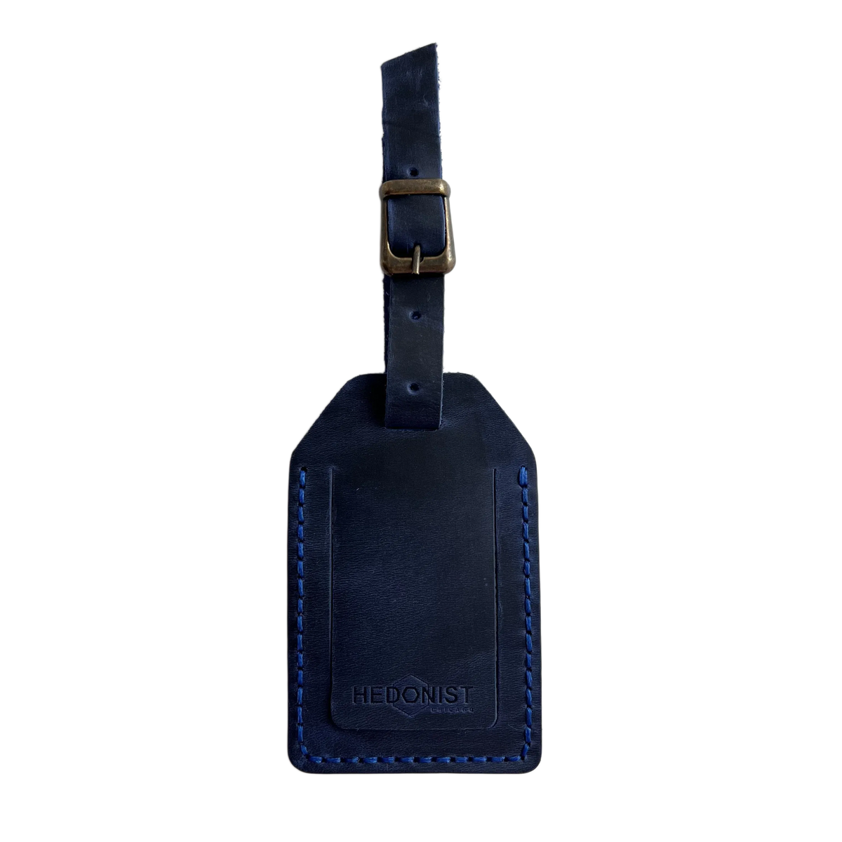 Navy blue full-grain leather luggage tag with matching strap and brass buckle, blue stitching, embossed Hedonist Chicago logo on the front, shown on an off-white background.