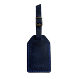 Navy blue full-grain leather luggage tag with matching strap and brass buckle, blue stitching, embossed Hedonist Chicago logo on the front, shown on an off-white background.