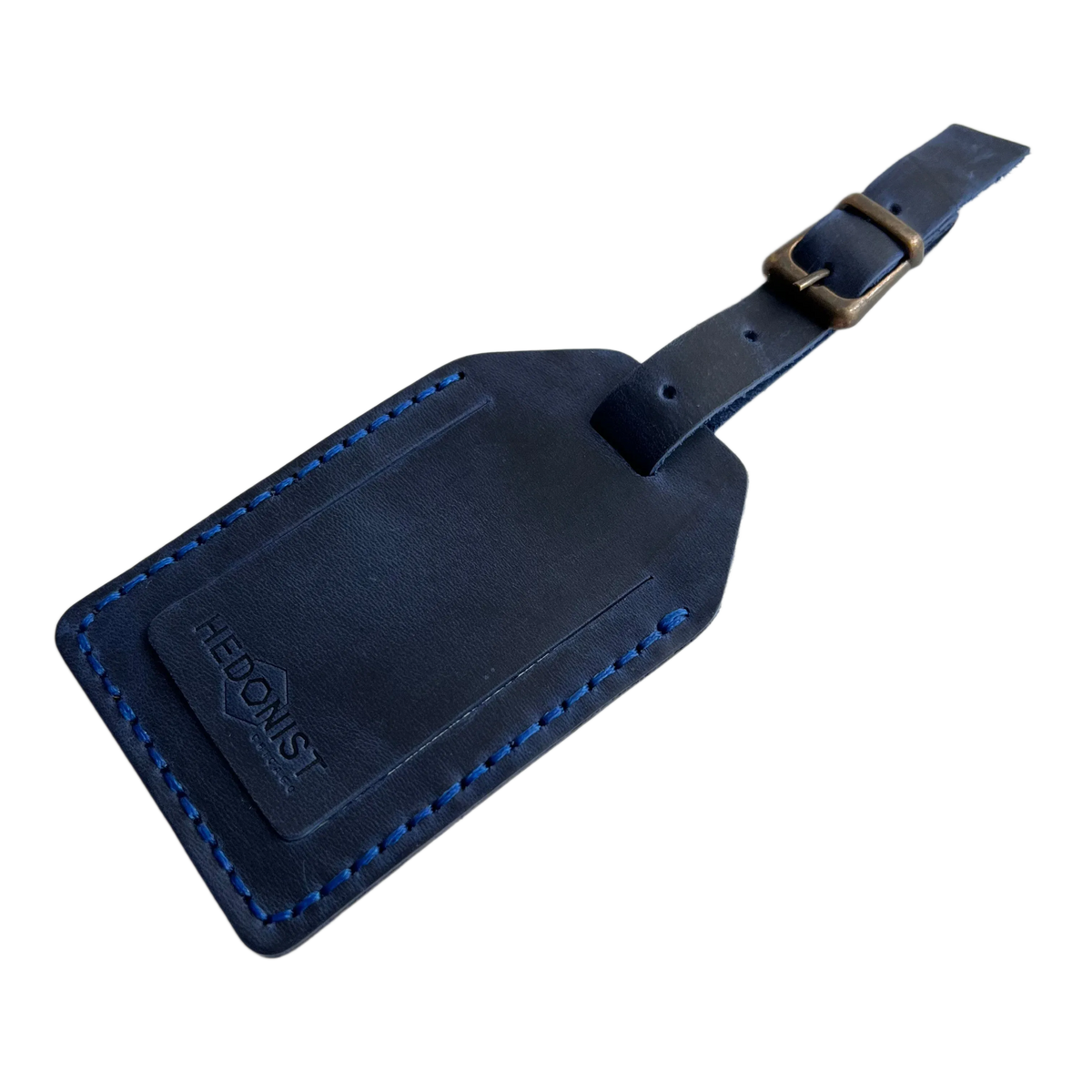 Navy blue full-grain leather luggage tag with bright blue stitching and brass buckle, embossed Hedonist Chicago logo on the front, shown on a light gray background.