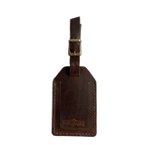 Brown full-grain leather luggage tag with brass buckle and strap, embossed Hedonist Chicago logo near the bottom, shown on a light gray background.