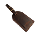Brown full-grain leather luggage tag with brass buckle strap, embossed Hedonist Chicago logo in the lower right corner, shown on a light gray background.