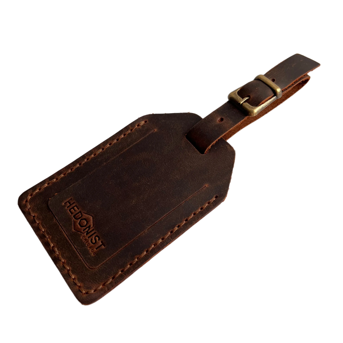 Brown full-grain leather luggage tag with matching leather strap and brass buckle, embossed Hedonist Chicago logo on the front, shown on a light gray background.