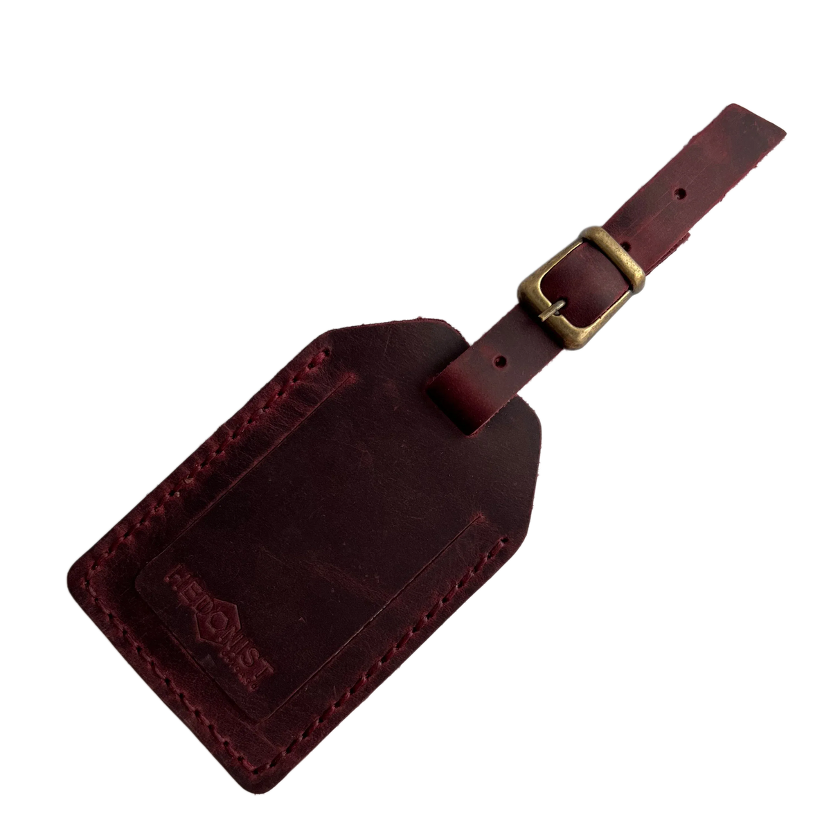 Burgundy full-grain leather luggage tag with brass buckle and strap, embossed Hedonist Chicago logo on the front, shown on a light background.