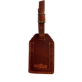 Cognac full-grain leather luggage tag with matching leather strap and brass buckle, embossed Hedonist Chicago logo on the front, shown on a light gray background.