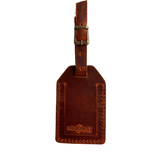 Cognac full-grain leather luggage tag with matching leather strap and brass buckle, embossed Hedonist Chicago logo on the front, shown on a light gray background.