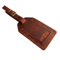Cognac full-grain leather luggage tag with matching leather strap and brass buckle, embossed Hedonist Chicago logo on the front, shown on a light gray background.