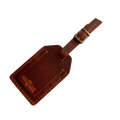 Cognac full-grain leather luggage tag with matching leather strap and brass buckle, embossed Hedonist Chicago logo on the front, shown on a light gray background.