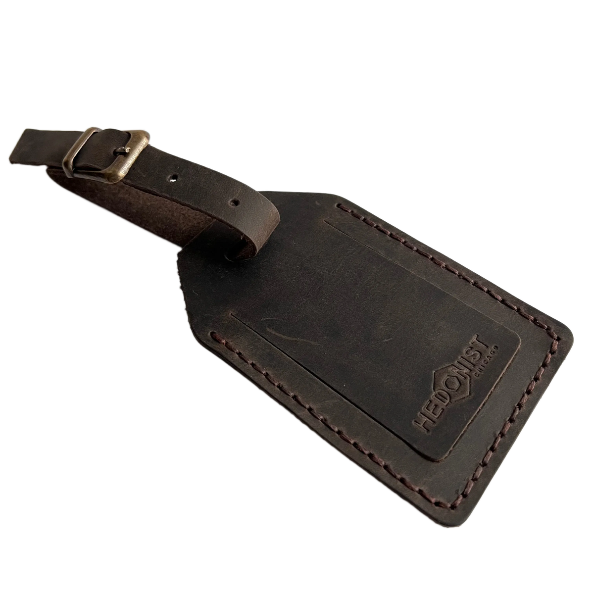 Dark brown full-grain leather luggage tag with matching leather strap and brass buckle, embossed Hedonist Chicago logo on the front, shown on a white background.