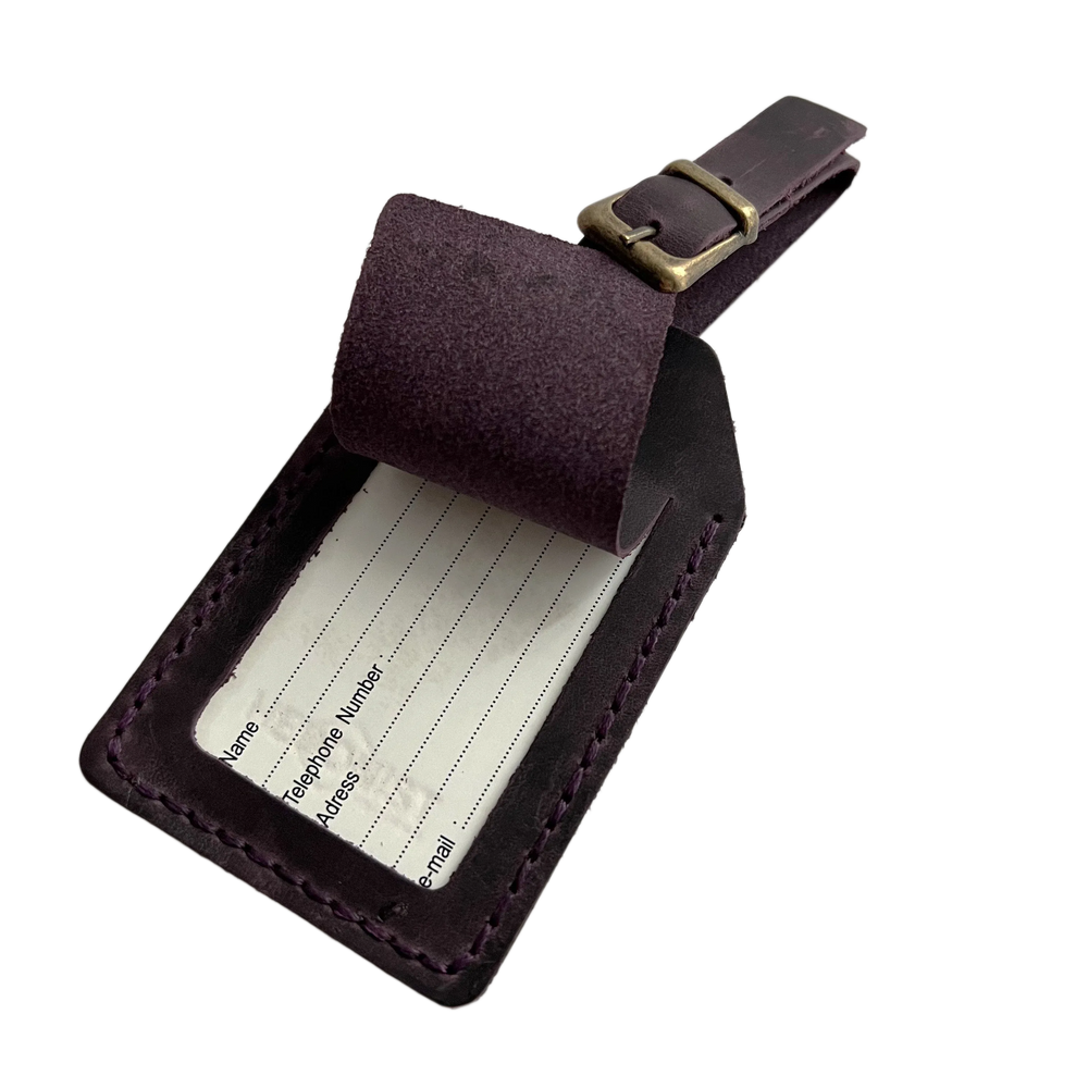 Plum full-grain leather luggage tag with matching adjustable strap and brass buckle, shown open to reveal a blank ID insert card, on a light background.