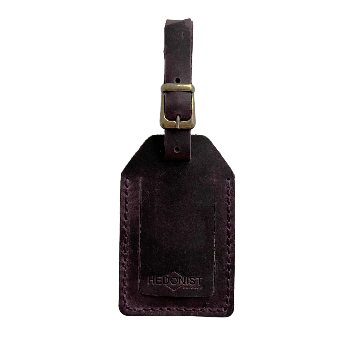 Plum full-grain leather luggage tag with brass buckle, embossed Hedonist Chicago logo on the front, shown on a light gray background.