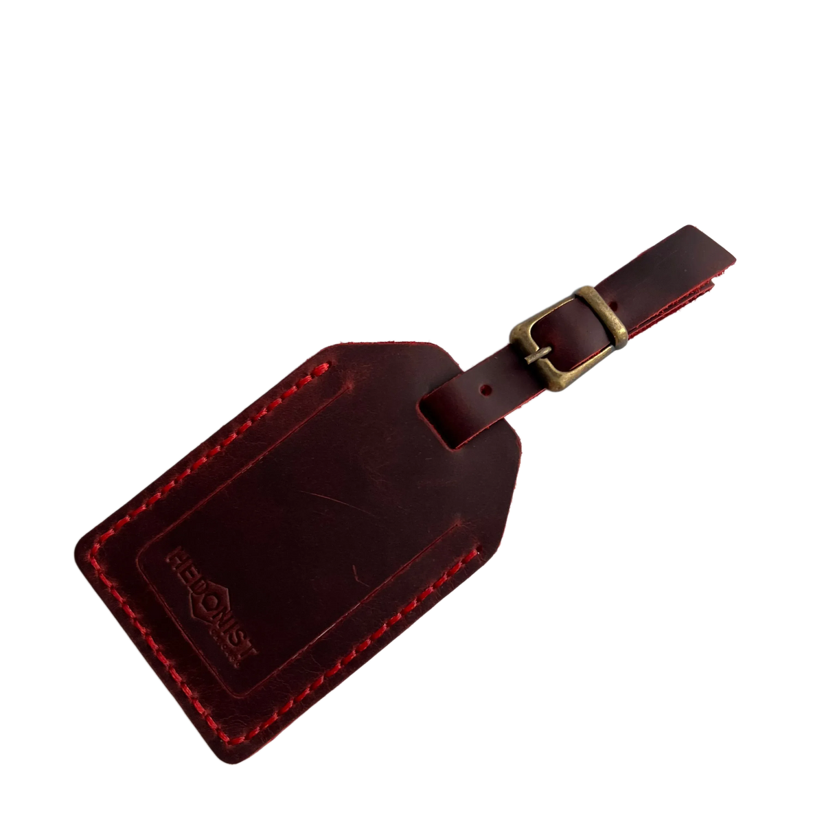 Red full-grain leather luggage tag with brass buckle, embossed Hedonist Chicago logo on the front, shown on a light gray background.