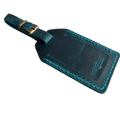 Teal full-grain leather luggage tag with brass buckle and matching teal stitching, embossed Hedonist Chicago logo on the front, shown on a light gray background.